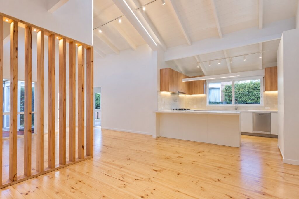 Open-plan kitchen and living area with a timber batten divider, pine flooring and lighting