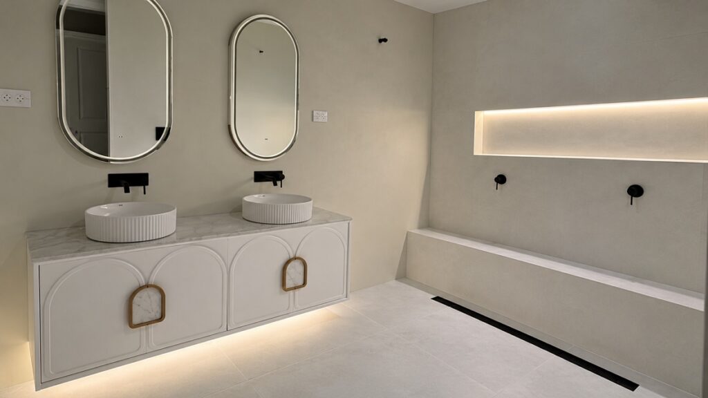 Double vanity with backlit oval mirrors and LED strip lighting in a wall recess