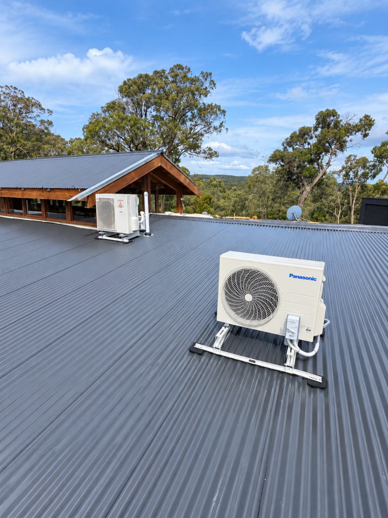 Two split system outdoor units mounted on stands on a metal roof