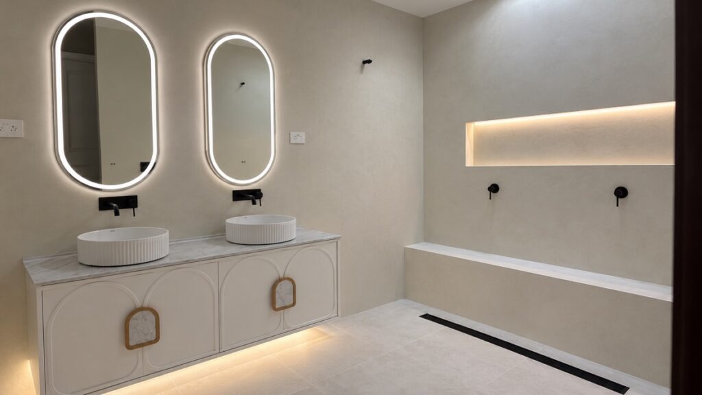 Double vanity with backlit oval mirrors, an LED-lit shower niche and under-vanity lighting