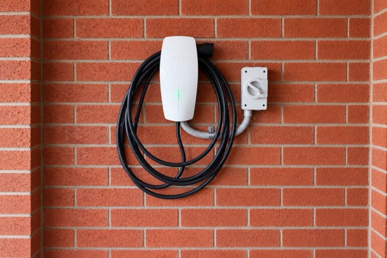 Wall-mounted EV charger with coiled charging cable and an isolator on a brick wall