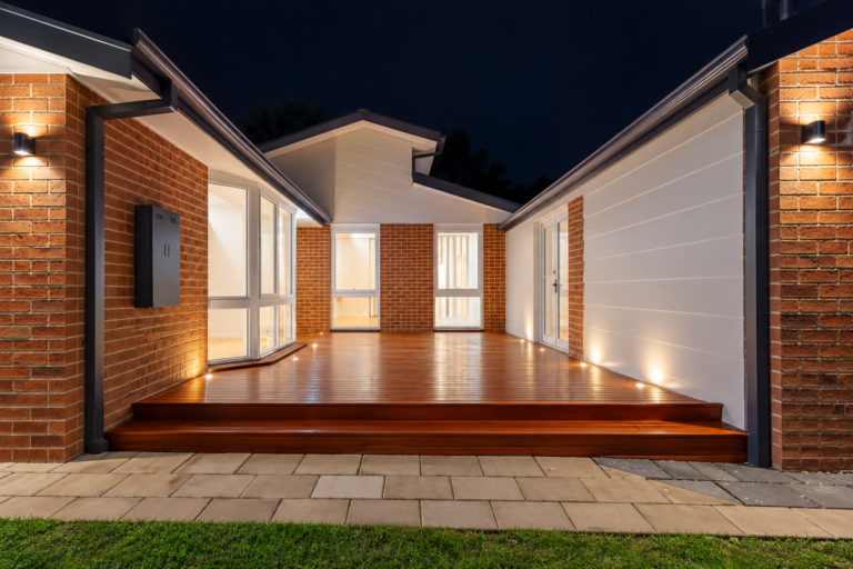 Home entry at night with wall lights either side and lit timber steps