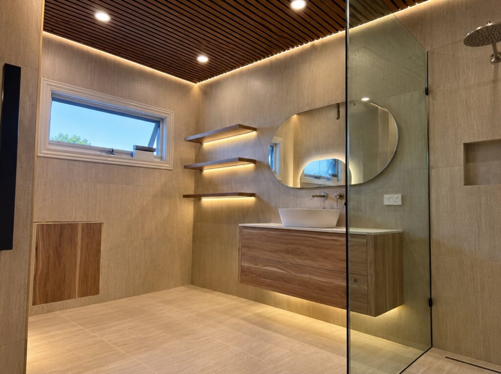 Renovated bathroom with LED strip lighting under floating shelves and the vanity, and a backlit round mirror