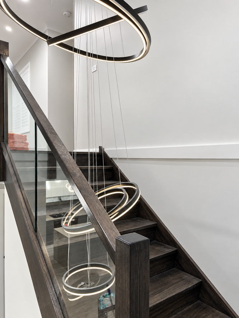 Staircase with glass balustrade and a tiered ring pendant light hanging through the stairwell