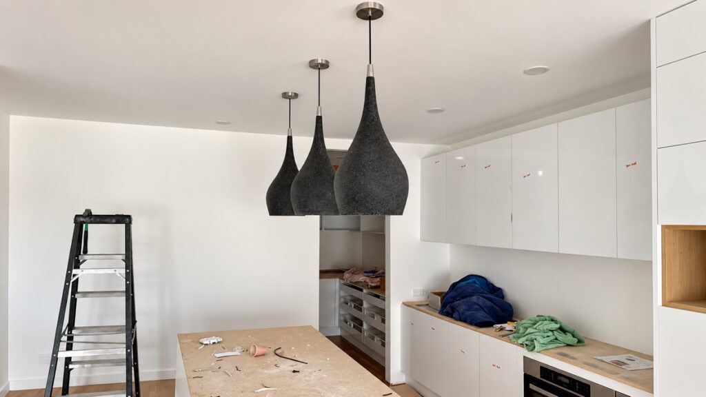 Black pendant lights being installed over a kitchen bench