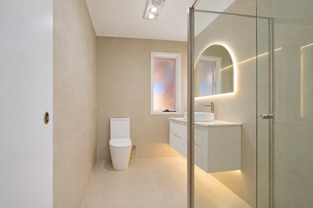 Renovated bathroom with a backlit arched mirror, LED under-vanity lighting and a ceiling heat, fan and light unit