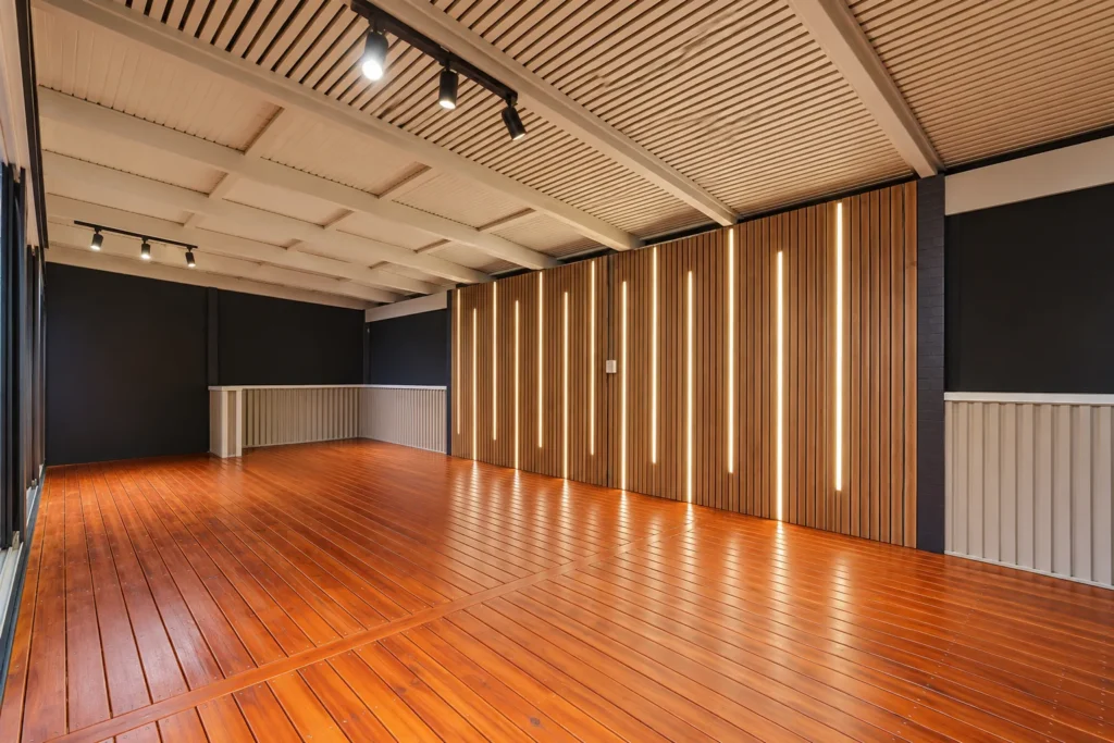 Covered deck with timber batten feature wall and vertical LED strip lighting above polished timber decking
