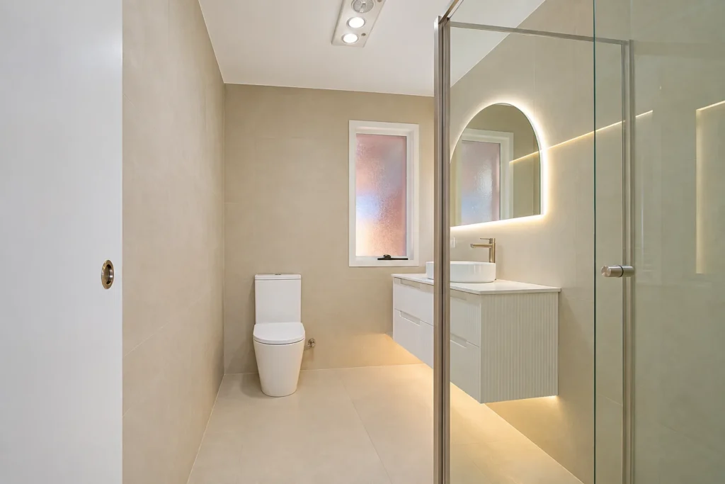 Renovated bathroom showing toilet, glass shower screen and fluted vanity with backlit mirror