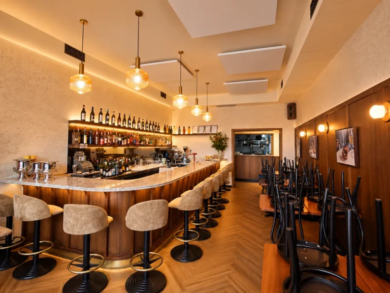 Hospitality venue with ribbed glass pendant lights over a curved bar, backlit bottle shelving and wall lights along the dining area
