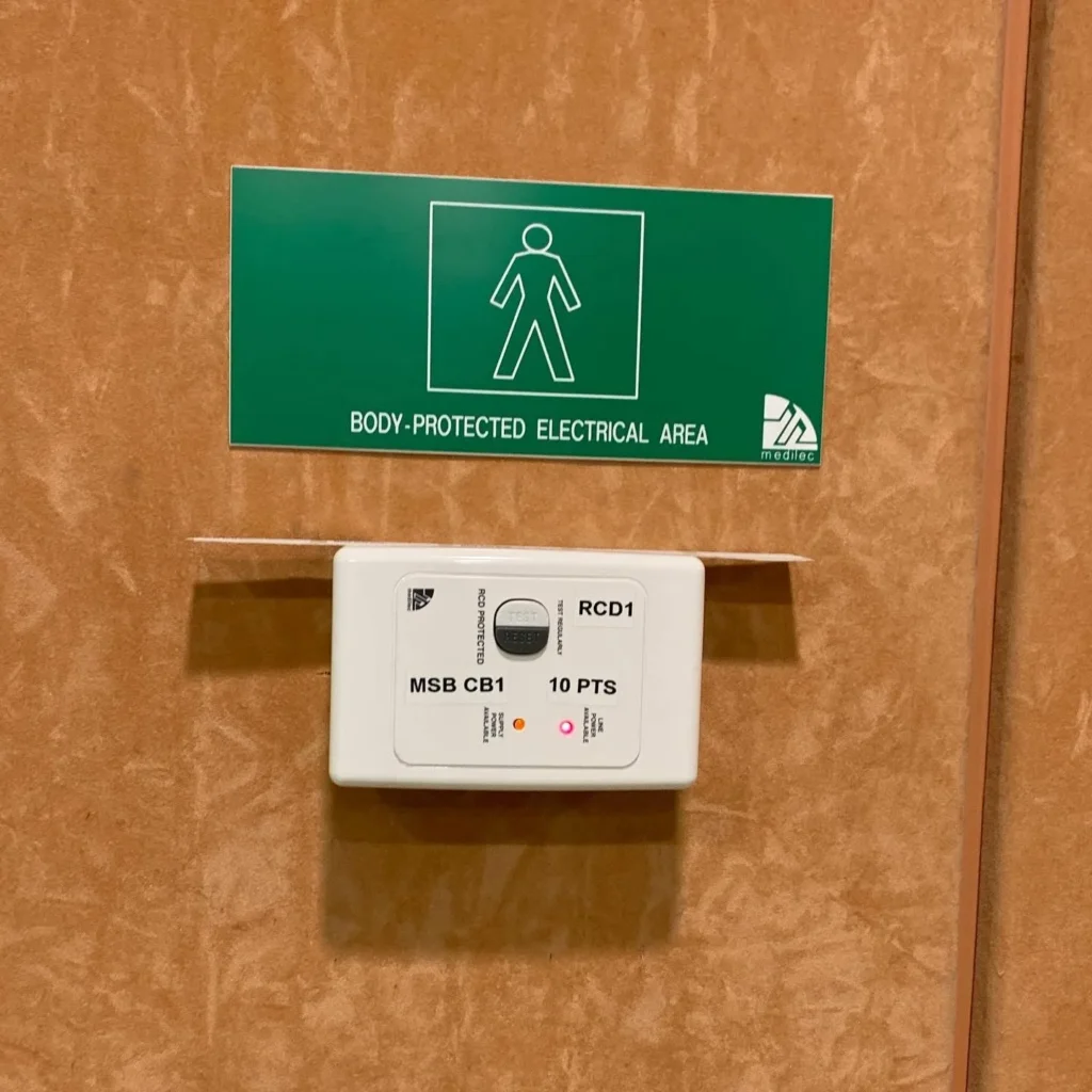 Body-protected electrical area sign above an RCD test panel in a clinical fit-out