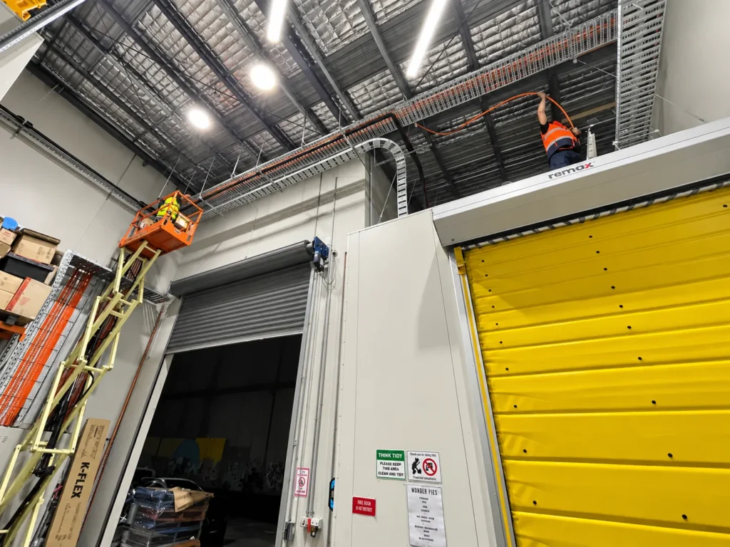 Cable tray and services run at high level above a roller door inside a warehouse