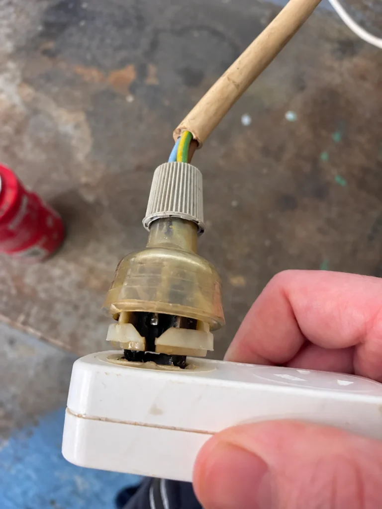 Heat-damaged plug top with charring inside, plugged into a powerboard