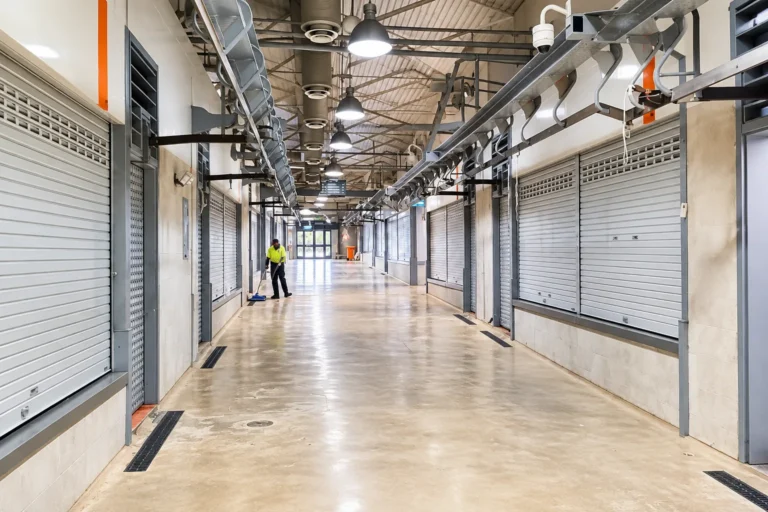Suspended pendant lighting installed above a commercial market aisle with roller shutter stalls