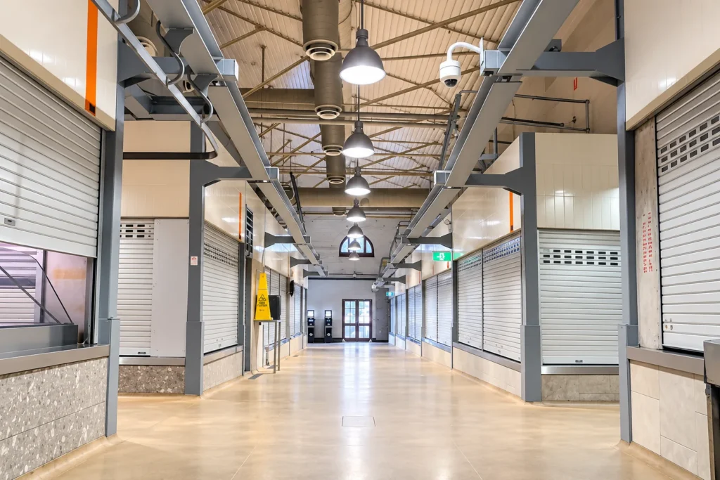 Market walkway lit by suspended pendant lights with exposed electrical services overhead