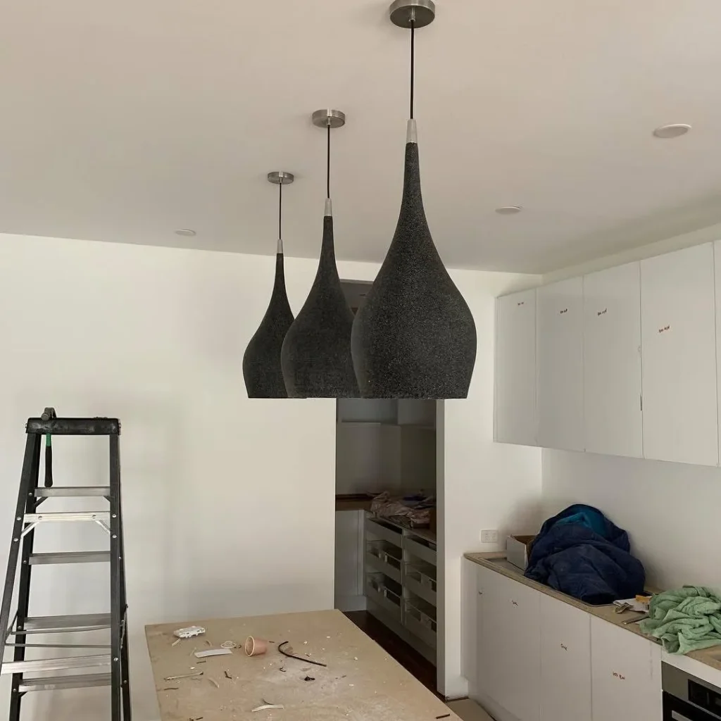 Three black pendant lights being installed over a kitchen bench